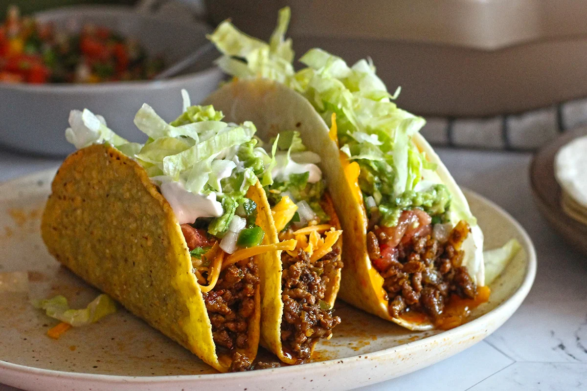 Three delicious looking tacos with cheese, beef, lettuce, and crunchy tortillas that have rounded bottoms.